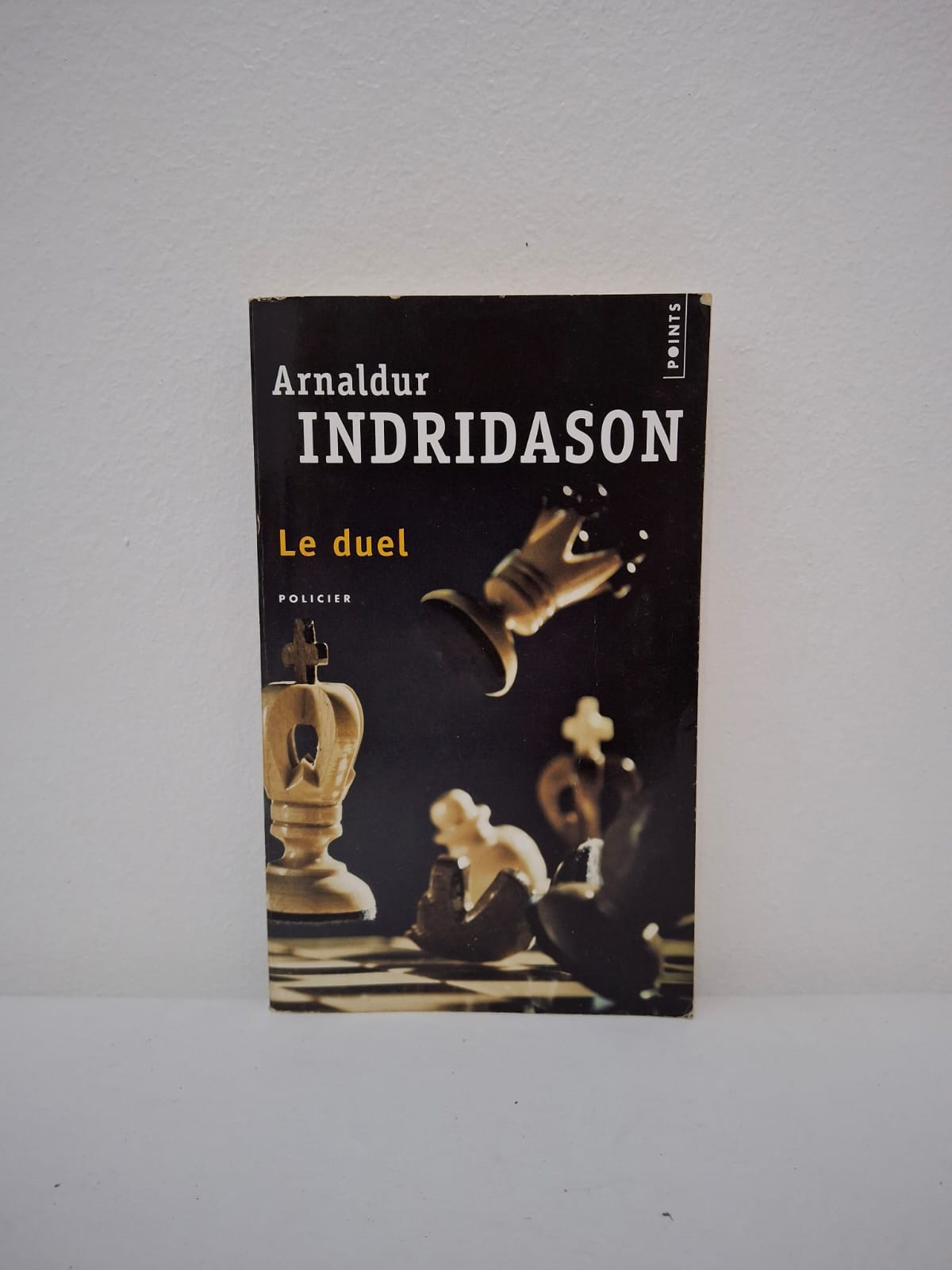 : Le Duel-Arnaldur Indriðason Alors que le monde entier a les yeux rivés sur le championnat du monde d'échecs, un jeune homme est retrouvé poignardé dans une salle de cinéma de la capitale islandaise. Le commissaire Marion Briem se charge d'une enquête complexe qui, sous l'apparence d'un simple fait divers, révèle des enjeux d'espionnage international entre l'Est et l'Ouest. Entre paranoïa politique et secrets du passé, le récit dépeint une atmosphère glaciale où chaque mouvement ressemble à une partie d'échecs mortelle. C'est une immersion fascinante dans l'Islande des années 70, marquée par les tensions diplomatiques et les drames intimes.